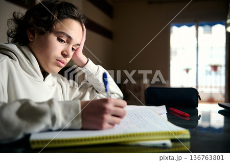 Teenage Boy Studying Homework at Night in Cozy Home Interior Focused and Thoughtful Teenage Boy Studying Homework at Night in Cozy Home Interior Focused and Thoughtful 136763801
