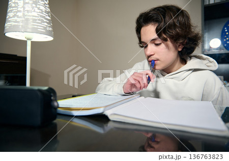 Teenage Boy Doing Homework At Home In Cozy Evening Study Session 136763823
