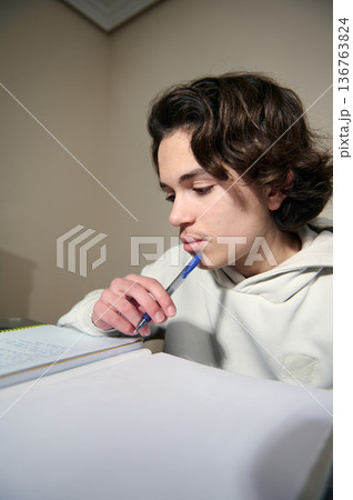 Teenage Boy Studying At Home Doing Homework In Cozy Evening Interior With Pen And Notebooks Teenage Boy Studying At Home Doing Homework In Cozy Evening Interior With Pen And Notebooks 136763824