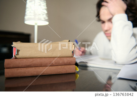Teenage Boy Studying Late At Home With Books Lamp And Notebook Looking Tired While Doing Homework Teenage Boy Studying Late At Home With Books Lamp And Notebook Looking Tired While Doing Homework 136763842