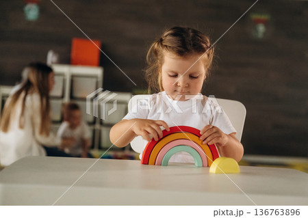 Girl is sitting and playing with toy. Group of children are in the kindergarten Girl is sitting and playing with toy. Group of children are in the kindergarten 136763896