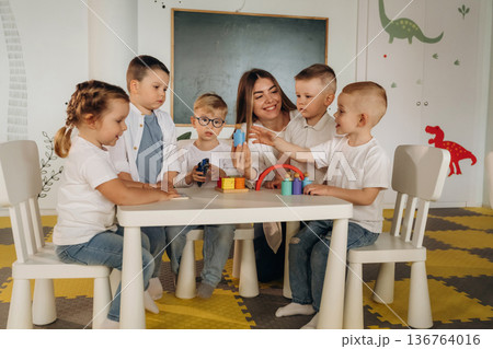 Sitting by the table. Children in kindergarten with their teacher 136764016