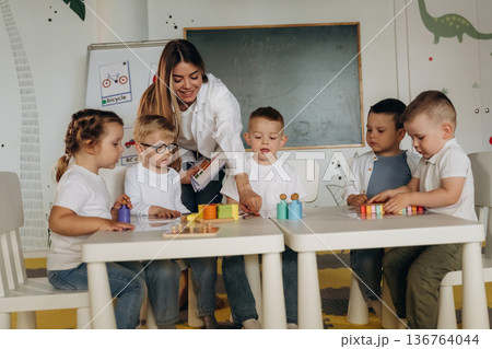 Smiling, learning, playing game by table. Children in kindergarten with their teacher 136764044
