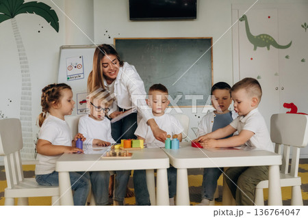 Smiling, learning, playing game by table. Children in kindergarten with their teacher Smiling, learning, playing game by table. Children in kindergarten with their teacher 136764047