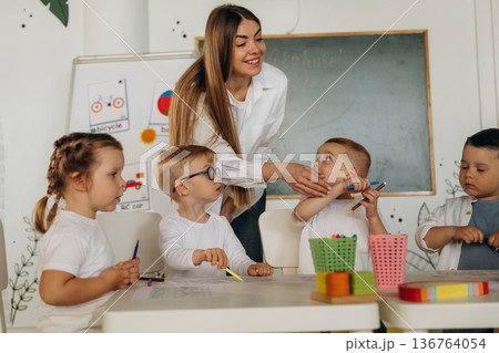 Drawing by the table. Children in kindergarten with their teacher Drawing by the table. Children in kindergarten with their teacher 136764054