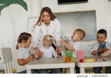 Drawing by the table. Children in kindergarten with their teacher Drawing by the table. Children in kindergarten with their teacher 136764055