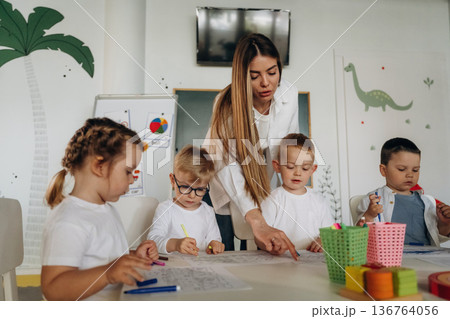 Drawing by the table. Children in kindergarten with their teacher 136764056