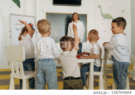 Raising hands, answering the question. Children in kindergarten with their teacher 136764064