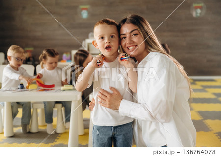 Boy and woman are standing together. Children in kindergarten with their teacher 136764078