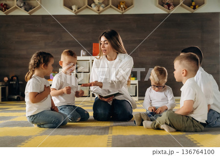 With book, sitting on the floor. Children in kindergarten with their teacher 136764100