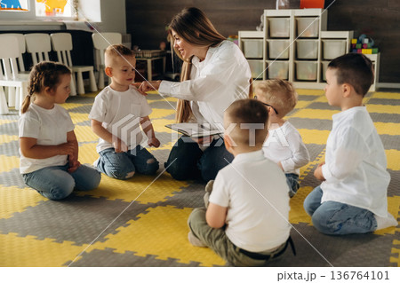 With book, sitting on the floor. Children in kindergarten with their teacher 136764101