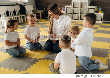 With book, sitting on the floor. Children in kindergarten with their teacher 136764102
