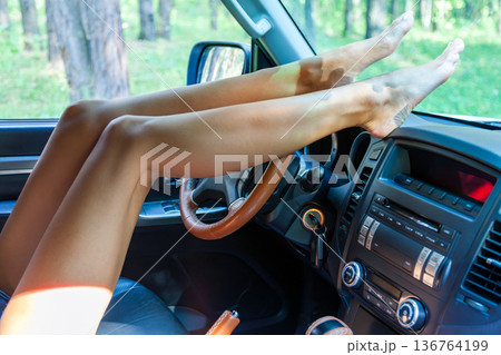 Long female legs on a steering wheel of a car 136764199