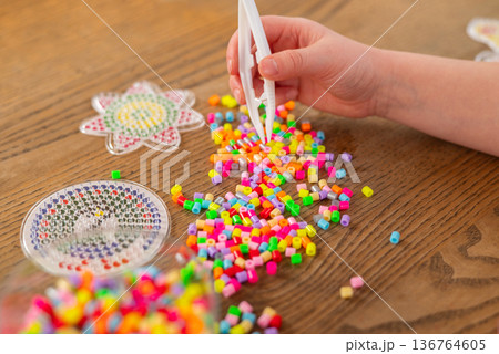 Child playing with colorful fuse beads at a wooden table. the creative process of making thermo mosaic art. Child playing with colorful fuse beads at a wooden table. the creative process of making thermo mosaic art. 136764605