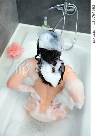 Beautiful young woman taking a bath with foam and washing her hair 136764662
