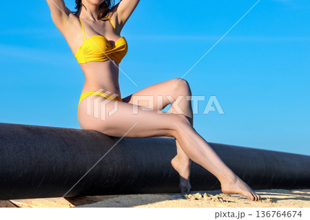 Beautiful young woman in a yellow swimsuit sitting on an oil pipeline 136764674