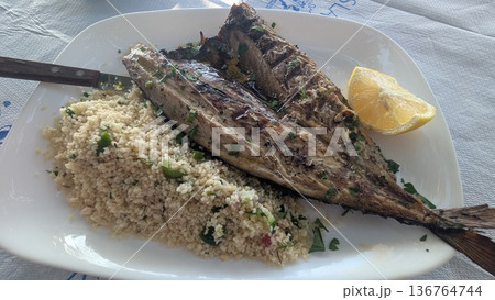 Grilled sun dried fish with couscous and a piece of cut lemon 136764744