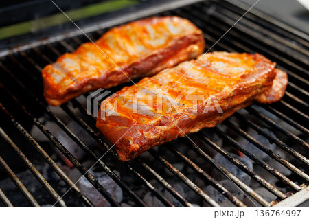Juicy ribs sizzling on the barbecue grill during a sunny afternoon gathering 136764997