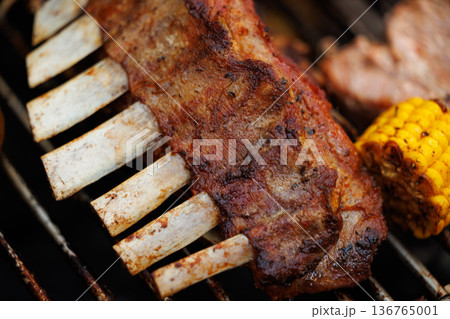 Delicious ribs sizzling on a grill with vibrant corn during a lively summer cookout Delicious ribs sizzling on a grill with vibrant corn during a lively summer cookout 136765001