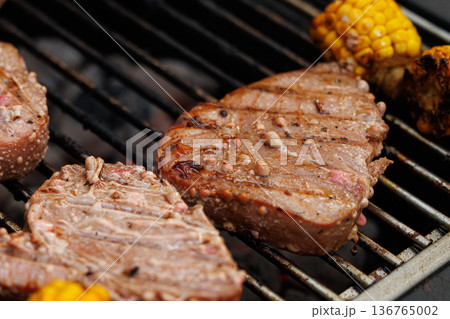 Juicy steaks and grilled corn cooking on a warm summer evening barbecue party Juicy steaks and grilled corn cooking on a warm summer evening barbecue party 136765002