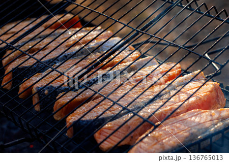 Grilling fresh salmon fillets over hot coals for a summer feast with friends and family Grilling fresh salmon fillets over hot coals for a summer feast with friends and family 136765013
