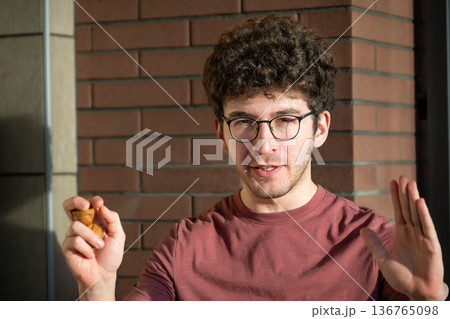 A young man with curly hair and glasses, contemplating a city view from a balcony, with buildings and distant mountains creating an urban background 136765098