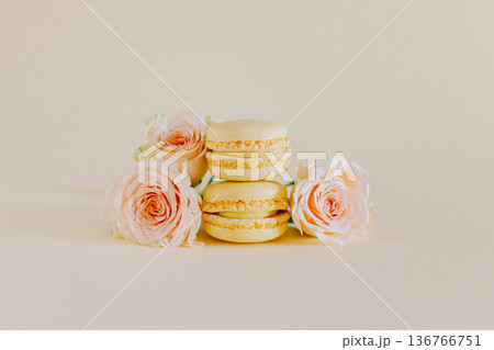 Tasty yellow french macarons with tender rose flowers on a peach pastel background. Tasty yellow french macarons with tender rose flowers on a peach pastel background. 136766751