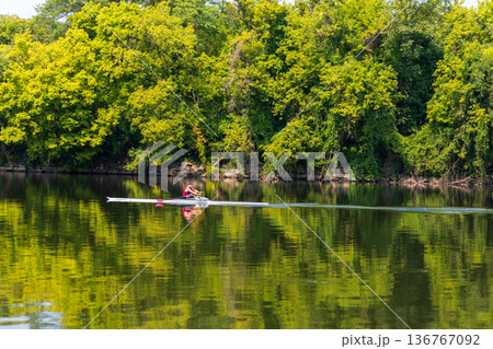 A man in a red boat is rowing across a lake 136767092