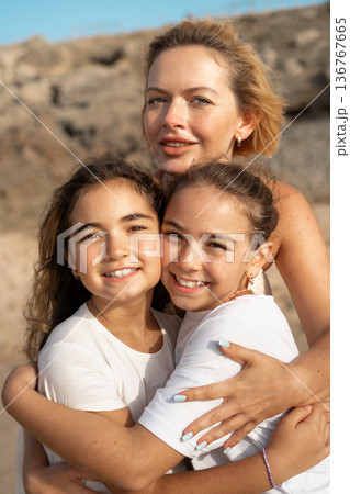 Loving mother embracing daughters on sandy beach 136767665