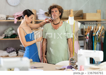 Woman tailor takes measurements from male client 136768781
