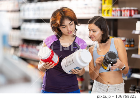 Woman and Latin girl consult about purchasing sports nutrition, enriched protein shake Woman and Latin girl consult about purchasing sports nutrition, enriched protein shake 136768825