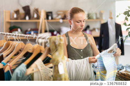 Girl chooses a set of clothes for summer. Visitor to the boutique examines the new summer collection of clothes Girl chooses a set of clothes for summer. Visitor to the boutique examines the new summer collection of clothes 136768832