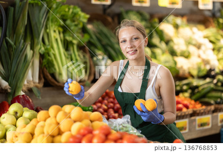 Young woman seller puts peaches in vegetable shop Young woman seller puts peaches in vegetable shop 136768853