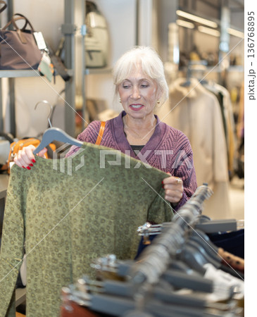retired woman stands in a store and chooses a jersey sweater retired woman stands in a store and chooses a jersey sweater 136768895