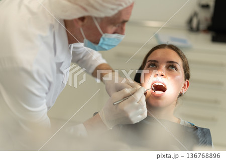 Mature man doctor dentist in white coat examines oral cavity of girl patient in dentistry. Mature man doctor dentist in white coat examines oral cavity of girl patient in dentistry. 136768896
