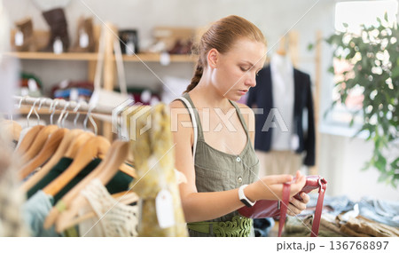 Young teen girl choosing a fashionable handbag in boutique Young teen girl choosing a fashionable handbag in boutique 136768897