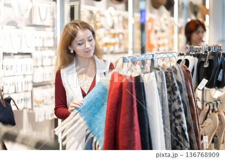 Young woman chooses scarf in accessories store Young woman chooses scarf in accessories store 136768909