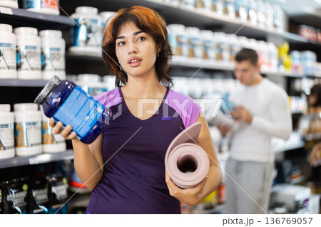 Young woman with yoga mat chooses sports nutrition Young woman with yoga mat chooses sports nutrition 136769057