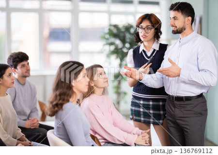 Male and female lecturer communicates with students, controls projector using remote control. Male and female lecturer communicates with students, controls projector using remote control. 136769112