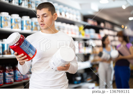 Young guy choosing protein powder jar in sports nutrition store 136769131
