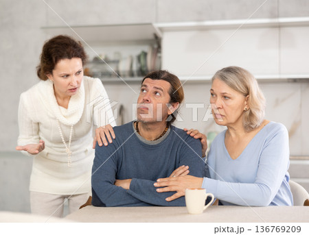 Senior woman sits near adult son and comforts him during quarrel with wife. 136769209