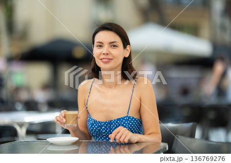 Smiling stylish brunette woman drinking espresso coffee while sitting on terrace of street cafe Smiling stylish brunette woman drinking espresso coffee while sitting on terrace of street cafe 136769276