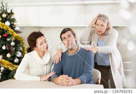 Mother on christmas eve is quarreling with her thinking adult son in kitchen, standing behind him, and wife hugs and calms him Mother on christmas eve is quarreling with her thinking adult son in kitchen, standing behind him, and wife hugs and calms him 136769291