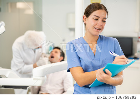 Young woman nurse in blue suit with paper is standing in dental office, clinic Young woman nurse in blue suit with paper is standing in dental office, clinic 136769292