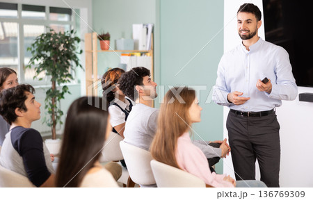 Male teacher explaining topic to students using digital board Male teacher explaining topic to students using digital board 136769309