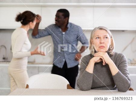 Elderly sad woman sits at table during family quarrel Elderly sad woman sits at table during family quarrel 136769323