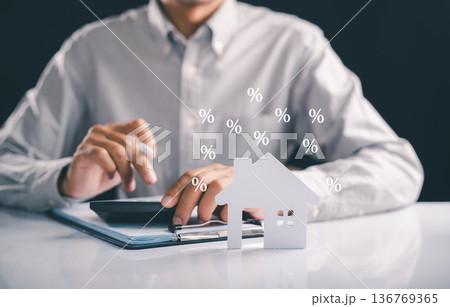Calculating real estate finance to invest, a person uses a calculator for tax and mortgage with percentage symbols floating suggesting property value, a home buying concept that grows the estate 136769365