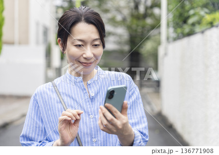 屋外でスマートフォンの画面を見る50代の女性 屋外でスマートフォンの画面を見る50代の女性 136771908