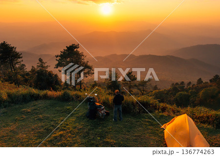 Solo traveler with motorcycle and camping tent enjoying sunset over mountain landscape. Solo traveler with motorcycle and camping tent enjoying sunset over mountain landscape. 136774263
