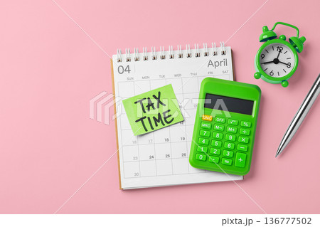 Tax time word on green sticky note on calendar with clock and calculator on pink background, financial and accounting planning, tax season, top view 136777502